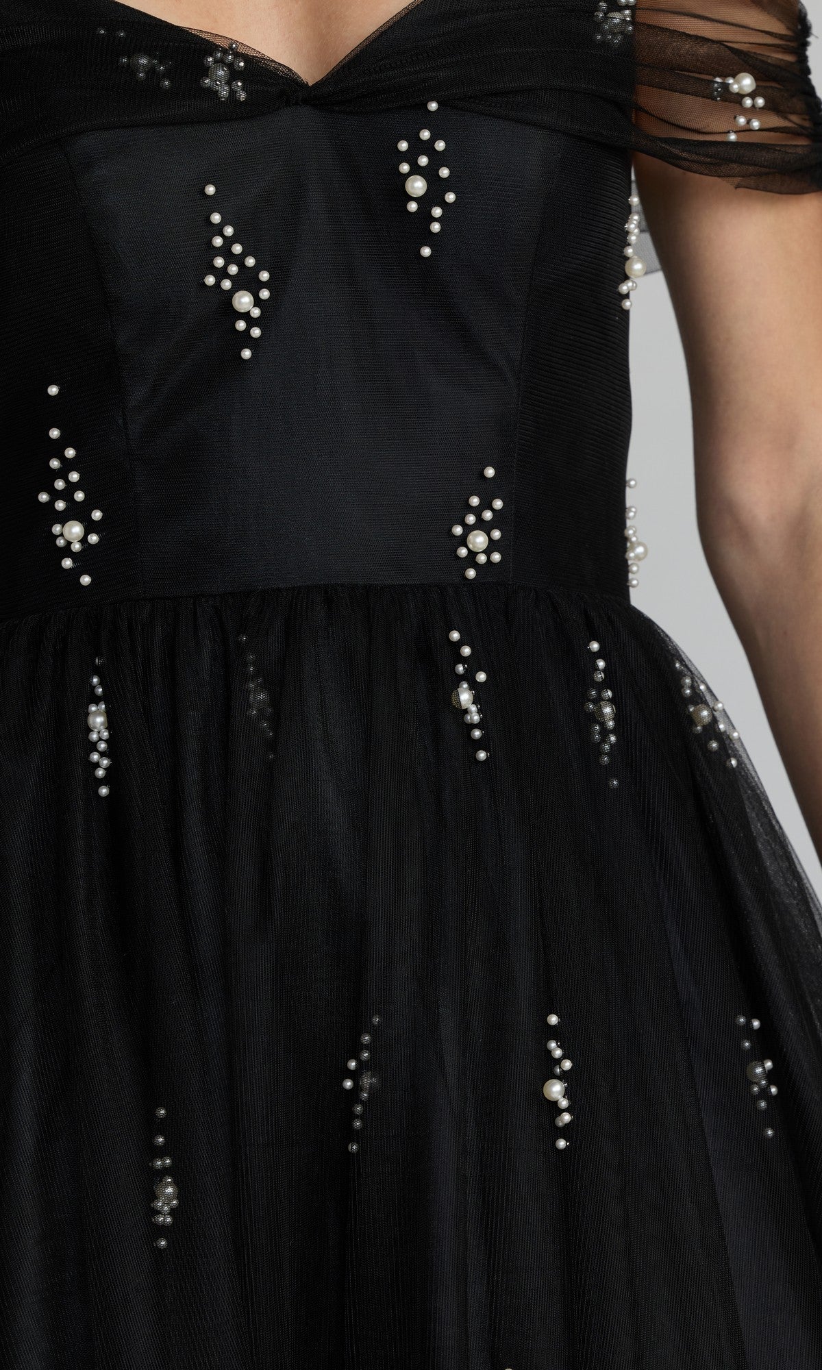 Close-up of the Long Formal Dress: Mac Duggal 13227 in black, featuring an off-shoulder neckline, sheer sleeves, and scattered pearl embellishments. The image highlights the bodice and upper skirt, showcasing the exquisite detailing of this elegant pearl embellished ballgown.
